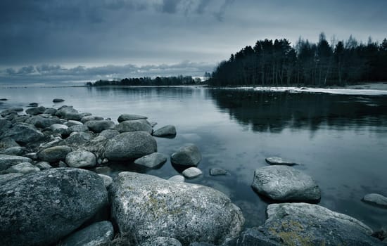 Seacoast in march with stones on the foreground on cloudy evening