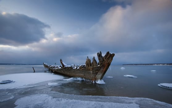 Old wooden shipwreck on frosty february at late evening