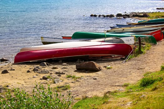 Various canoes chained up on a sandy shore.