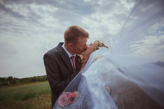 Beautiful bride and groom standing in grass and kissing. Wedding couple fashion shoot.
