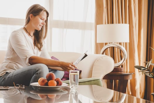 Mature woman is relaxing on a couch in her apartment with a magazine
