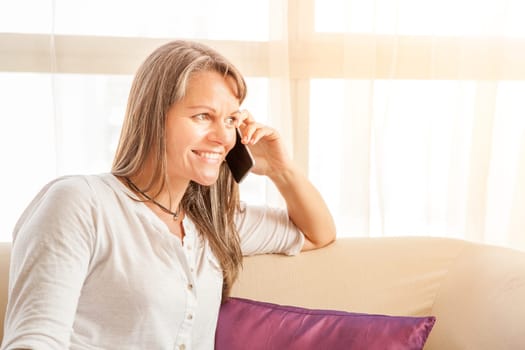 Mature attractive woman is talking on her cell phone at home