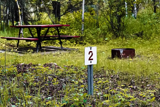Number 2 self registration camping site marker with a picnic table and fire pit in the background.