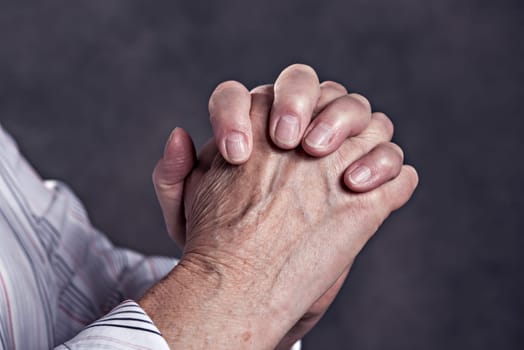 wrinkly hands of  elderly woman praying in front of dark background