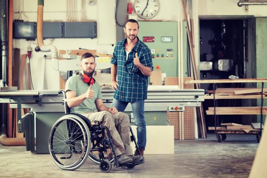 disabled worker in wheelchair in a carpenter's workshop with his colleague showing thumb up