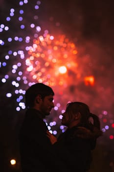 A silhouette of a kissing couple in front of a huge fireworks display. Filtered image with grain