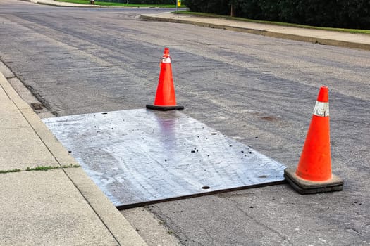 A steel plate on the road with construction pylons.