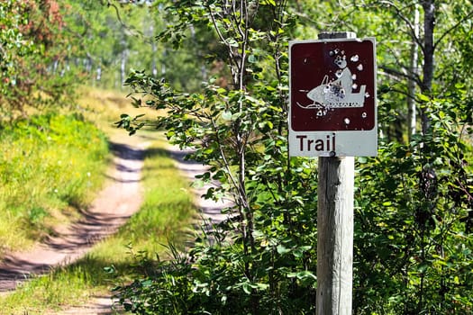 A shot up trail sign with a road in the distance.