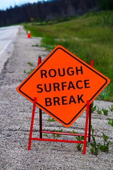 An orange rough surface break sign with construction pylons behind it.
