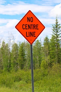 A no centre line sign with trees in the background.