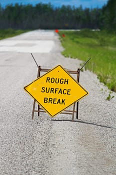 A yellow rough surface break sign with a road blurring into the background.
