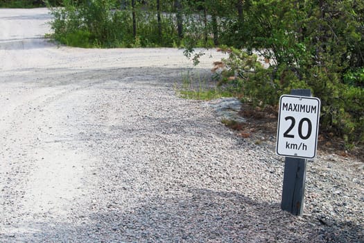 A maximum 20 km per hour sign along a gravel road.