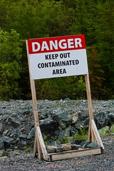 A danger keep out of contaminated area sign on rocky ground.