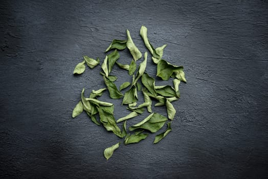 Top view dried curry leaves, Indian cuisine spices on dark background.