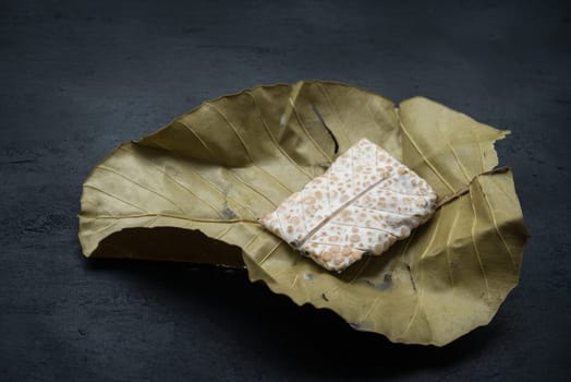 Fresh raw tempeh wrapped in leaf on dark background. Traditional Indonesian food made from fermented soy bean.
