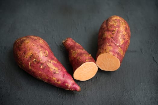 Raw orange sweet potatoes over dark table. Close up.