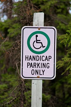 A handicap parking only sign with trees in the background.