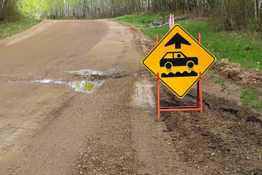 A bumpy road ahead sign with a large pothole.