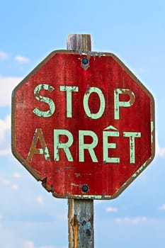 An old stop sign in both french and english against a blue sky.