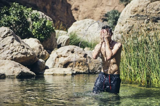 Young man splashing water on face. Refreshing in Wadi Shab, Sultanate of Oman.
