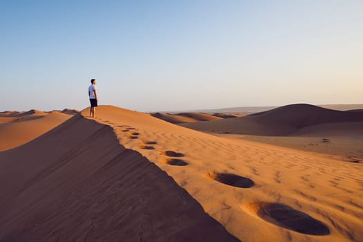 Young man standing on top of sand dune and looking at view. Desert Wahiba Sands in Oman.