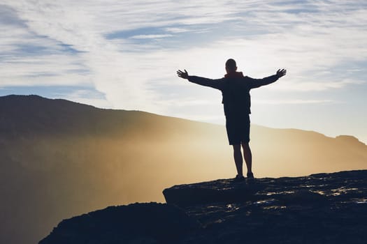 Silhouette of happy tourist on the edge of cliff at sunrise. Jebel Akhdar, Grand Canyon of Oman.