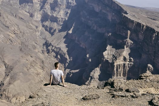 Young tourist resting on the edge of cliff. Jebel Akhdar, Grand Canyon of Oman