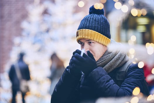 Young man drinking mulled wine. against illuminated christmas trees. Munich, Germany.