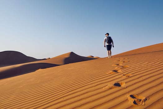 Young tourist with backpack walking on sand dune. Desert Wahiba Sands in Oman.