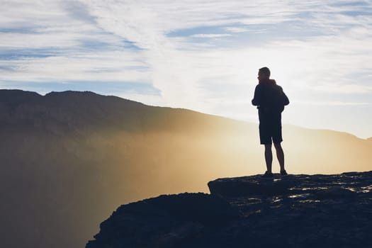 Silhouette of young tourist on the edge of cliff at sunrise. Jebel Akhdar, Grand Canyon of Oman.