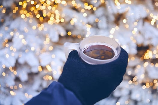 Man holding cup of mulled wine against illuminated christmas tree.  Munich, Germany.