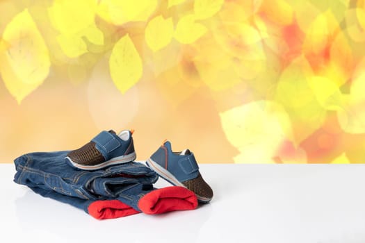 Colorful children jeans clothes.  Fashionable red lined thermojeans and a trendy pair of blue sneakers on bright table over abstract yellow autumn background. Autumn and winter jeans fashion. Space for your display product montage.