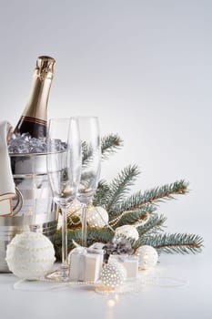 Still life with cooled champagne bottle standing in a bucket with ice, two champagne flutes and Christmas ornaments on a gray background, Christmas and New Year celebration