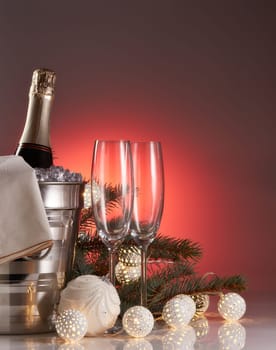 Still life with champagne bottle standing in a bucket with ice, two empty champagne flutes, LED lights garland and Christmas ornaments. Christmas and New Year celebration background