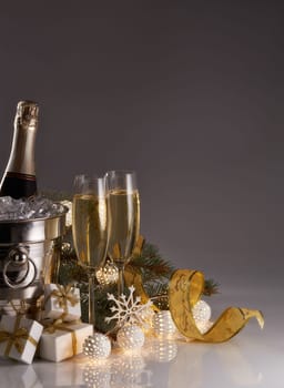Still life with champagne bottle standing in a bucket with ice, two full champagne flutes, LED lights garland and Christmas ornaments. Christmas and New Year celebration background