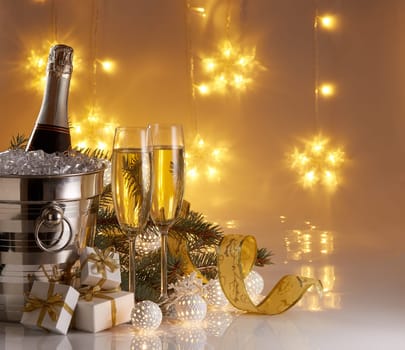Still life with champagne bottle standing in a bucket with ice, two full champagne flutes, LED lights garland and Christmas ornaments. Christmas and New Year celebration background