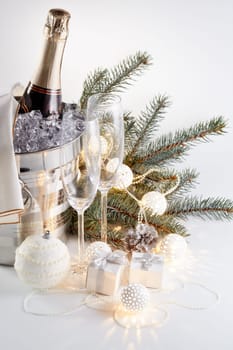 Still life with cooled champagne bottle standing in a bucket with ice, two champagne flutes and Christmas ornaments on a gray background, Christmas and New Year celebration