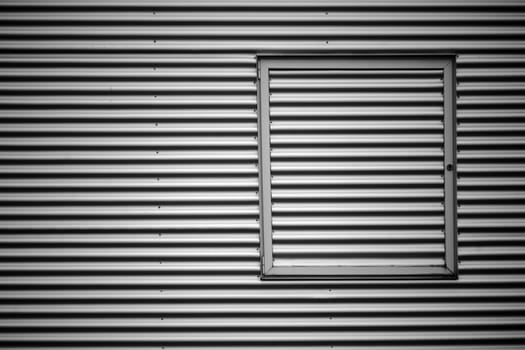 The closeup of the corrugated iron facade of an industrial building with a metal window frame..
