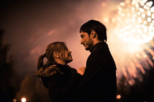 A silhouette of a kissing couple in front of a huge fireworks display. Filtered image with grain