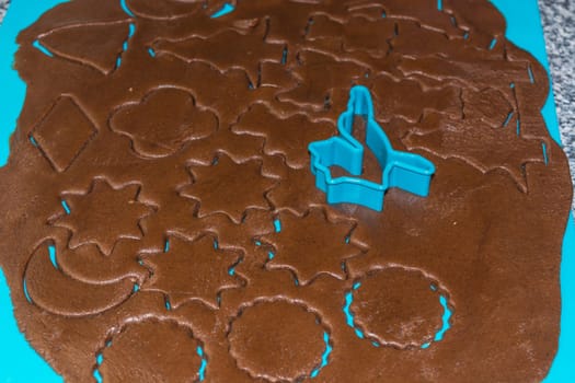 Raw dough is being punched out for the holiday cookies on a blue underlay. Preparing gingerbread cookies. Steps to making biscuits. Top view.