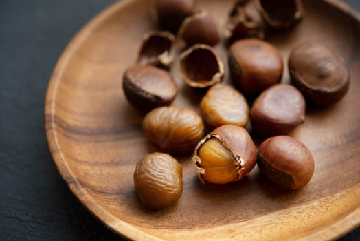 Chestnuts on wooden plate on dark background.