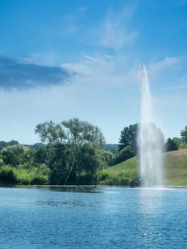 Fountain on the banks of the Havel with grass hills and trees in sunny summer weather.