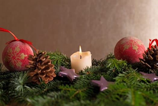 christmas decor with tree-balls, candle, branch and cone in front of golden background