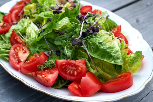 mixed summer salad on plate and wooden ground
