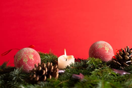 christmas decor with tree-balls, candle, branch and cone in front of red background