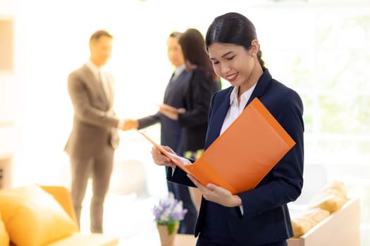 Portrait of Asian Businesswoman hold working file with business team in background using for coporate background work