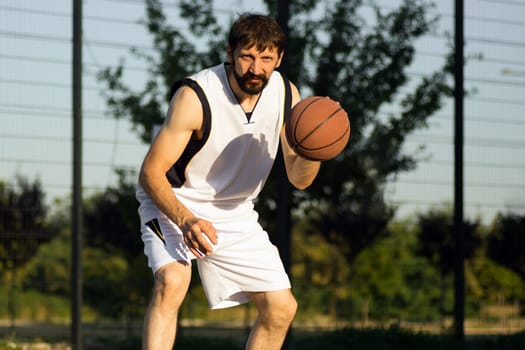 The basketball player is playing basketball or streetball at the street outdoors.