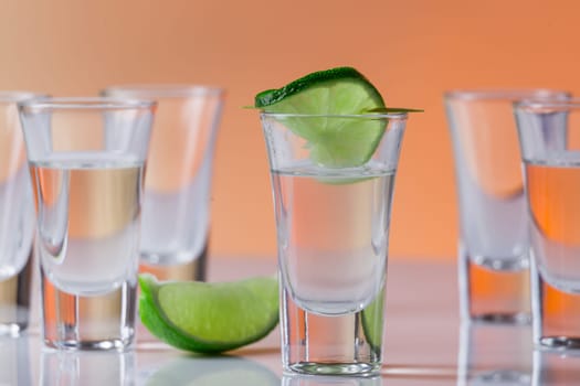 Tequila shot with a slice of lime on the glass on orange background. Selective Focus