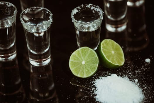 Tequila with lime and salt on black background
