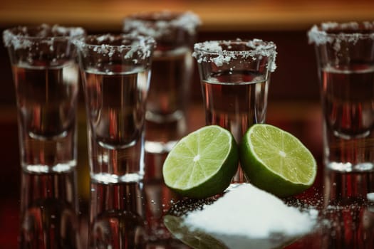 two shots of tequila with lime and salt on a wooden table bar on the background of bright lights of the bar